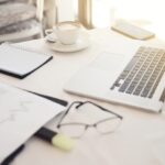 Foreground of objects on the working place: eyeglasses, diagrammes, laptop, notebook